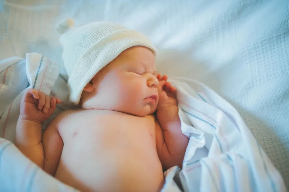 A newborn in a white knit hat sleeping on a blanket