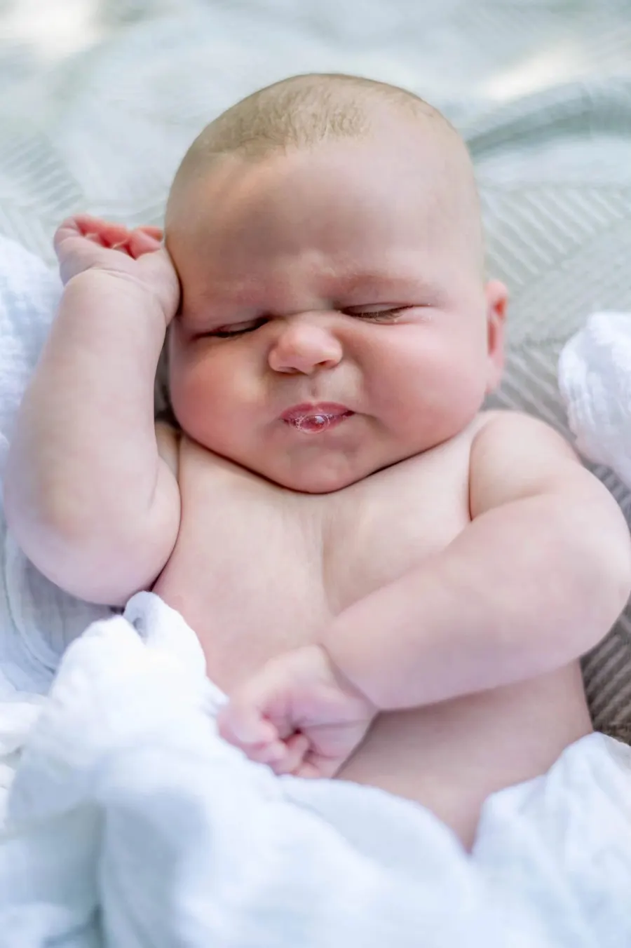 A sleeping newborn stretched out on a soft white blanket