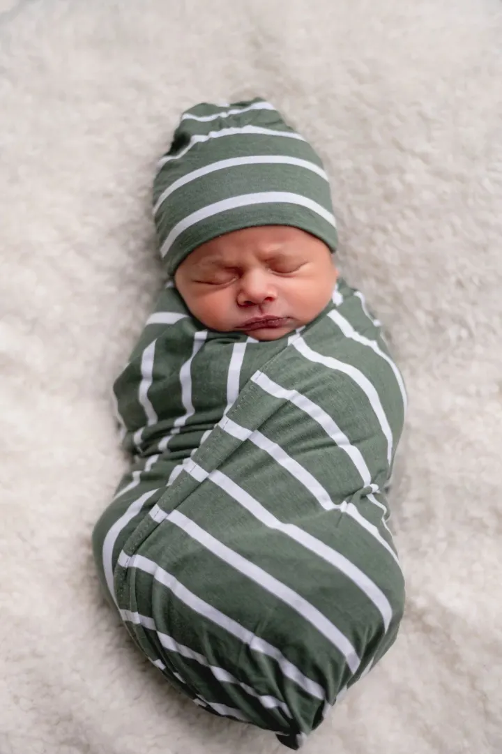 A swaddled newborn in a striped wrap and hat, asleep